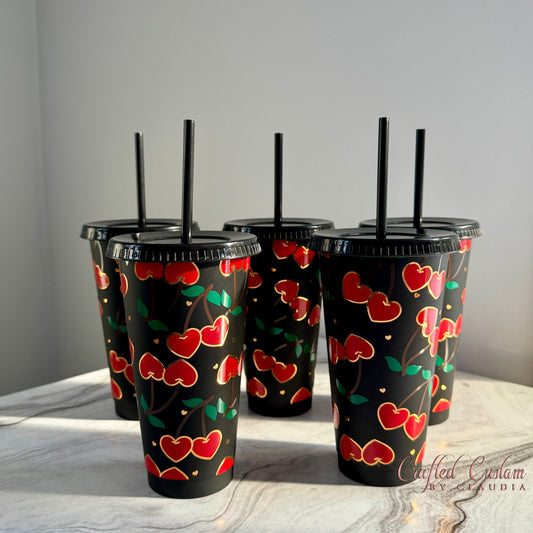 A set of black plastic cold cups with a red and gold cherry pattern and straws.