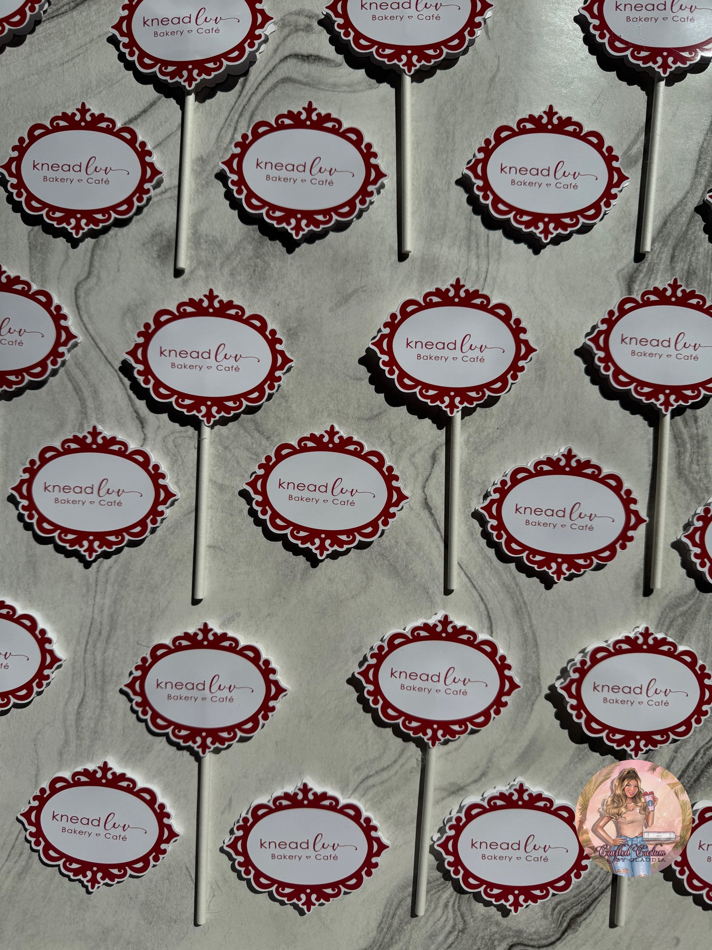 Pattern of 'knead luv' branding on cupcake toppers against a gray marble background.