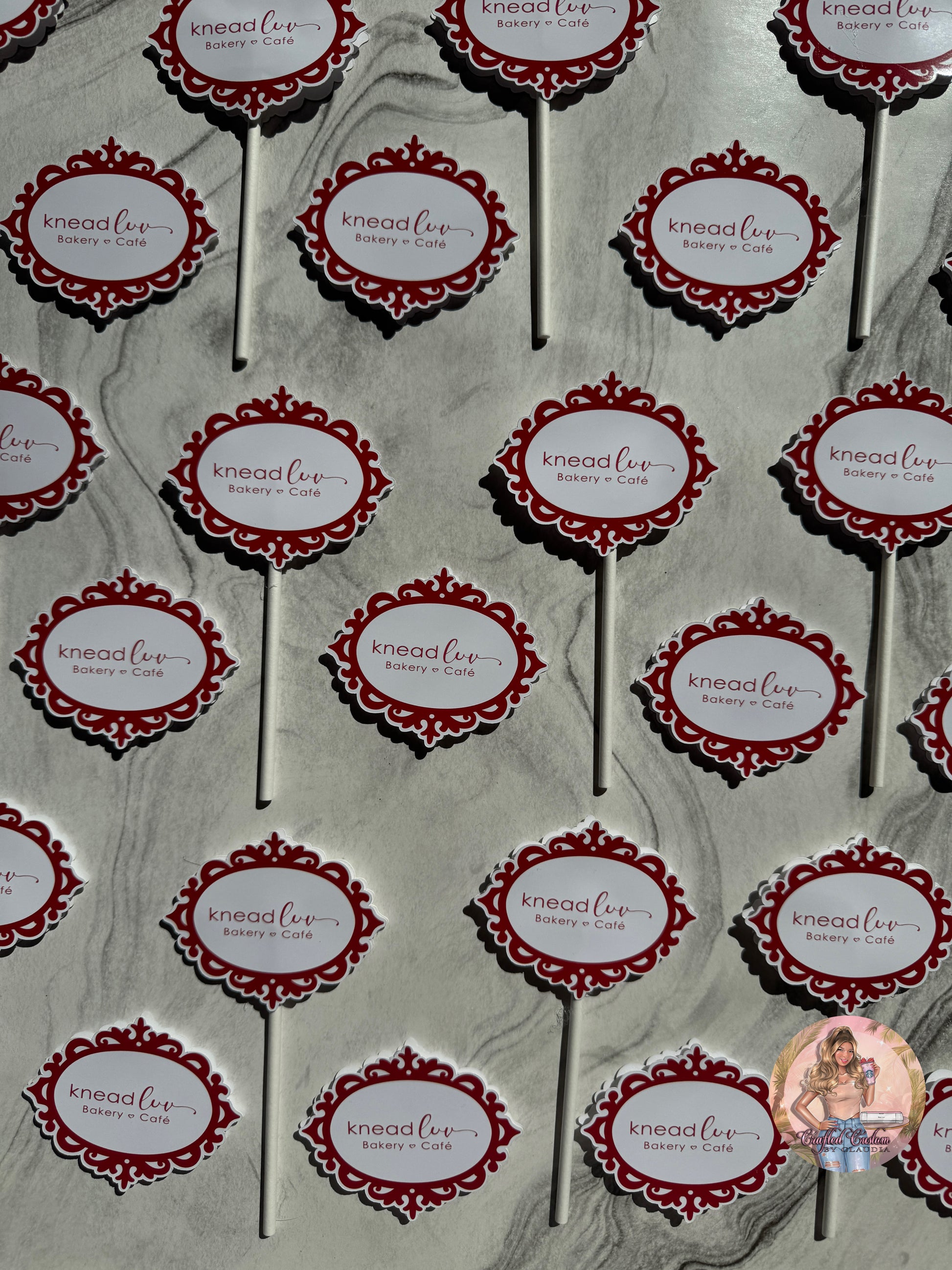 Pattern of 'knead luv' branding on cupcake toppers against a gray marble background.