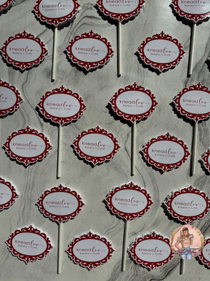 Pattern of 'knead luv' branding on cupcake toppers against a gray marble background.