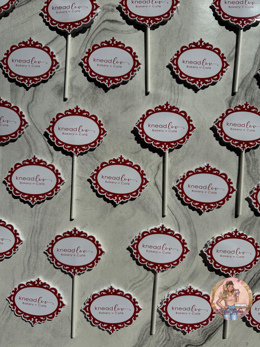 Pattern of 'knead luv' branding on cupcake toppers against a gray marble background.