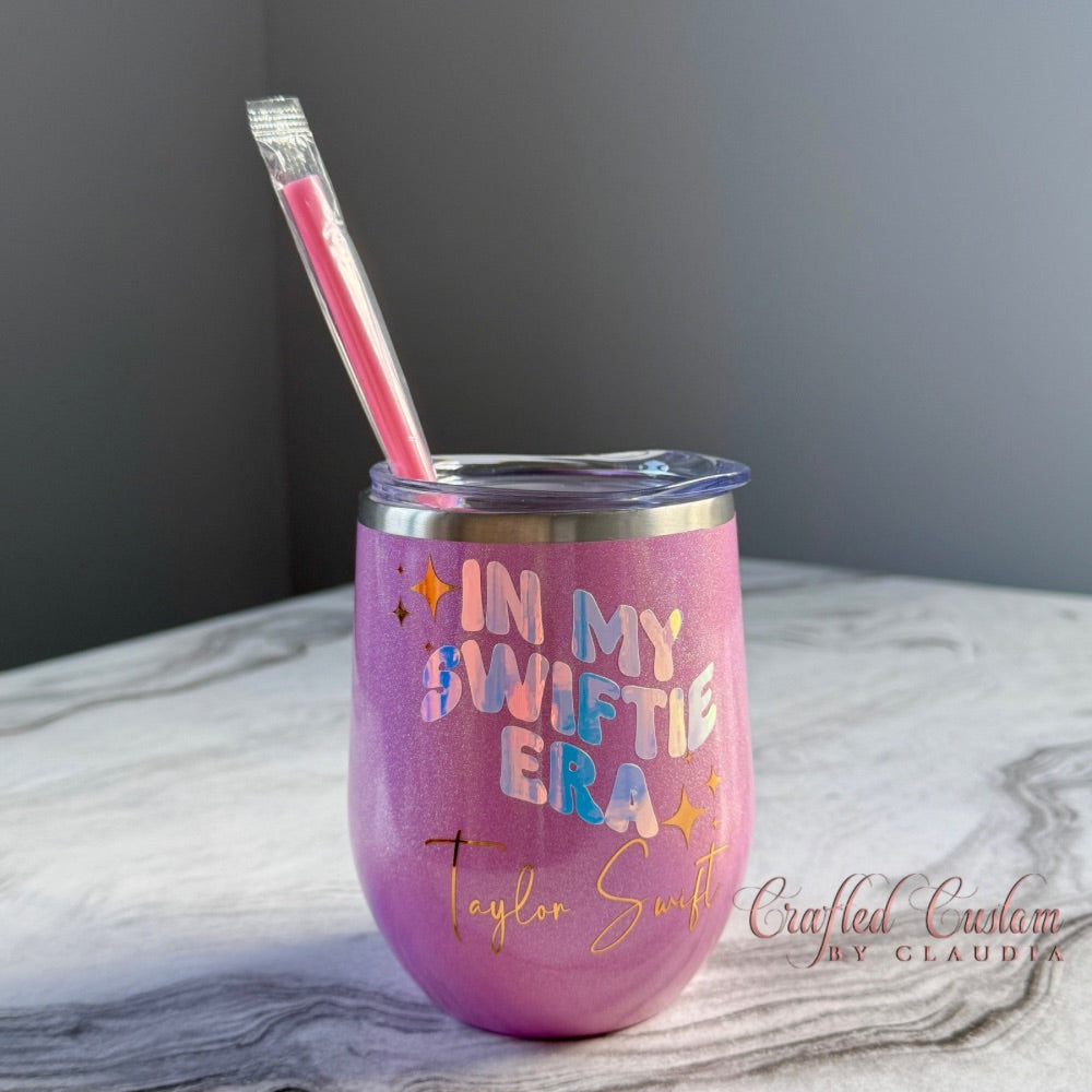 Pink tumbler with 'In My Swiftie Era' text and straw on a marble surface